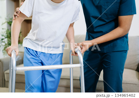 Closeup view of patient using walker during physical therapy with healthcare professional support, showing recovery, rehabilitation, and mobility training care. 134965402
