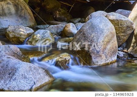 Smooth River Rocks and Flowing Water with Sunlight in Natural Forest Setting 134965928