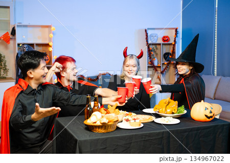 Friends in spooky Halloween costumes enjoy drinks and food at a festive indoor party with pumpkins, red cups, and laughter. 134967022