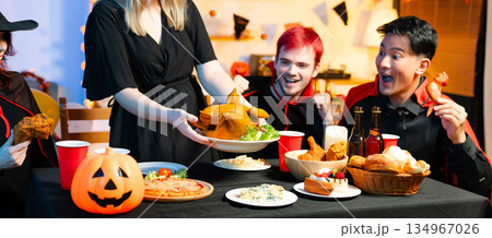 Friends in spooky Halloween costumes enjoy drinks and food at a festive indoor party with pumpkins, red cups, and laughter. Friends in spooky Halloween costumes enjoy drinks and food at a festive indoor party with pumpkins, red cups, and laughter. 134967026