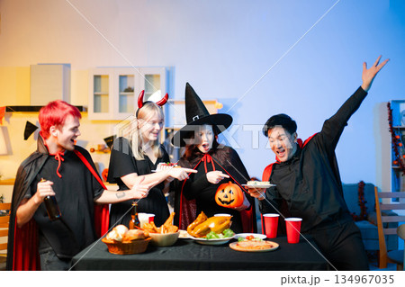 Group of young friends in Halloween costumes enjoy food and drinks at a cozy indoor party. with fun, spooky vibes, red cups, and pumpkin decor. Group of young friends in Halloween costumes enjoy food and drinks at a cozy indoor party. with fun, spooky vibes, red cups, and pumpkin decor. 134967035