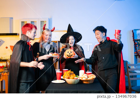 Group of young friends in Halloween costumes enjoy food and drinks at a cozy indoor party. with fun, spooky vibes, red cups, and pumpkin decor. Group of young friends in Halloween costumes enjoy food and drinks at a cozy indoor party. with fun, spooky vibes, red cups, and pumpkin decor. 134967036
