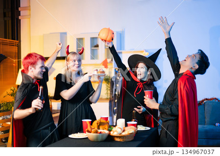 Group of young friends in Halloween costumes enjoy food and drinks at a cozy indoor party. with fun, spooky vibes, red cups, and pumpkin decor. 134967037