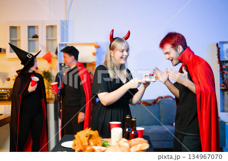 Group of young friends in Halloween costumes enjoy food and drinks at a cozy indoor party. with fun, spooky vibes, red cups, and pumpkin decor. 134967070