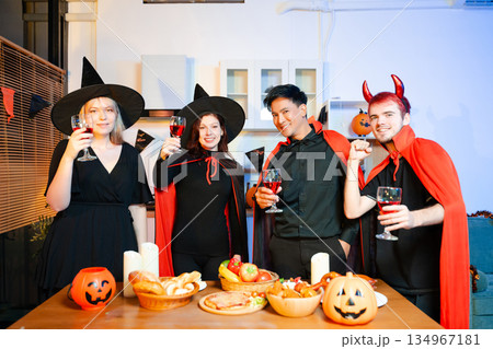 Halloween costumes toast with red wine at a festive indoor party. Pumpkins, food, and celebration set the mood for fun, spooky vibes and seasonal cheer. Halloween costumes toast with red wine at a festive indoor party. Pumpkins, food, and celebration set the mood for fun, spooky vibes and seasonal cheer. 134967181