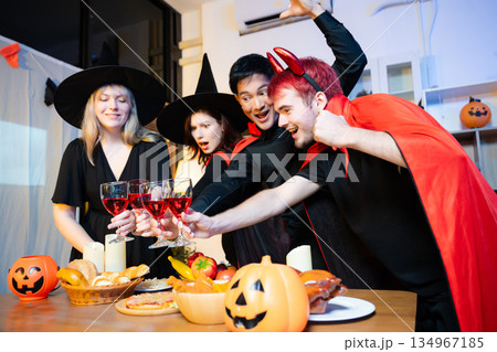 Halloween costumes toast with red wine at a festive indoor party. Pumpkins, food, and celebration set the mood for fun, spooky vibes and seasonal cheer. Halloween costumes toast with red wine at a festive indoor party. Pumpkins, food, and celebration set the mood for fun, spooky vibes and seasonal cheer. 134967185