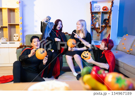 Halloween costumes toast with red wine at a festive indoor party. Pumpkins, food, and celebration set the mood for fun, spooky vibes and seasonal cheer. 134967189