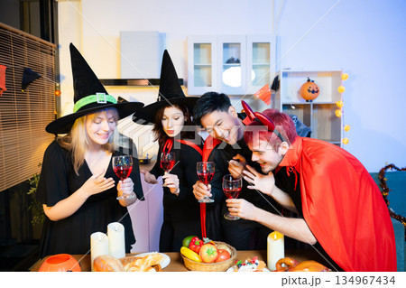 Halloween costumes toast with red wine at a festive indoor party. Pumpkins, food, and celebration set the mood for fun, spooky vibes and seasonal cheer. 134967434