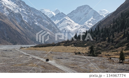 Vehicle driving through rugged mountain landscape with snow-capped peaks 134967774