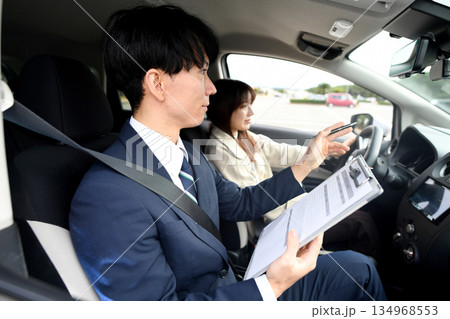 自動車教習所で指導するアジア人の男性教官と若い女性 自動車教習所で指導するアジア人の男性教官と若い女性 134968553