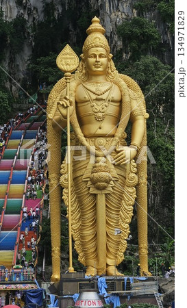 Lord Murugan golden statue stands majestically before rainbow stairs and limestone cliffs, radiating spiritual grandeur, cultural pride, and natural beauty at Malaysia iconic Batu Caves temple. 134971829