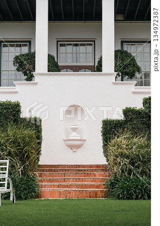 Classic white stucco facade of a building with brick stairs, lush green lawn 134972387