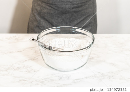 A whisk placed in a glass mixing bowl containing sifted powdered sugar, ready for the preparation of Simple White Royal Icing. 134972581