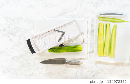 Freshly sliced cucumber laid out on paper towels for moisture removal, part of the Mini Cucumber Sandwiches recipe. Ideal for food prep illustrations or healthy snack tutorials. 134972582