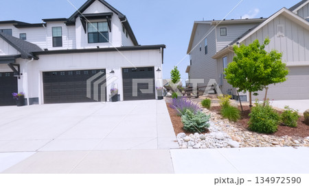 Two attached homes with dark garage doors are shown with a wide, clean concrete driveway. The front yards are landscaped with low shrubs and decorative rocks. Two attached homes with dark garage doors are shown with a wide, clean concrete driveway. The front yards are landscaped with low shrubs and decorative rocks. 134972590