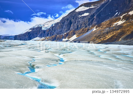 Athabasca Glacier Crevasses and Rocky Mountain Slopes Under Blue Sky 134972995