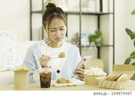 リビングでスマホを見ながらカロリーを気にしてお弁当を食べる若い日本人女性 リビングでスマホを見ながらカロリーを気にしてお弁当を食べる若い日本人女性 134973487