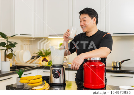 Young Asian man drinking protein banana cottage cheese milk shake in home kitchen after workout diet Young Asian man drinking protein banana cottage cheese milk shake in home kitchen after workout diet 134973986