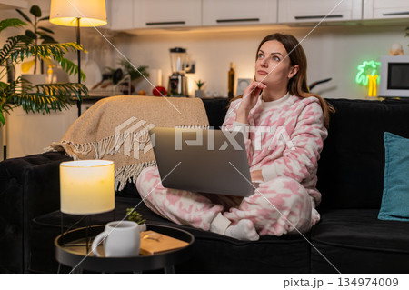 Adult woman with laptop at night deep in thought during remote work online session focused calm deep 134974009