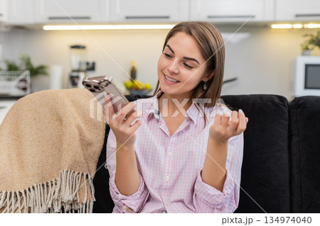 Young woman on smartphone speaker talks with friend or coworker listens nods and laughs during call 134974040