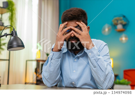 Indian man buries face in palms feeling burnout stressed severe emotional exhaustion moment indoors Indian man buries face in palms feeling burnout stressed severe emotional exhaustion moment indoors 134974098