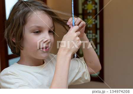 Young boy styling his brown hair with a pencil at home. Candid childhood portrait 134974208