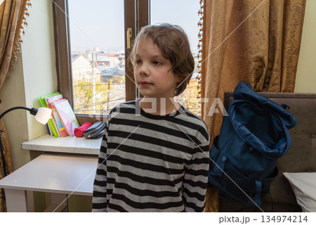 Young schoolboy in his room by the window. Child with backpack ready for school Young schoolboy in his room by the window. Child with backpack ready for school 134974214