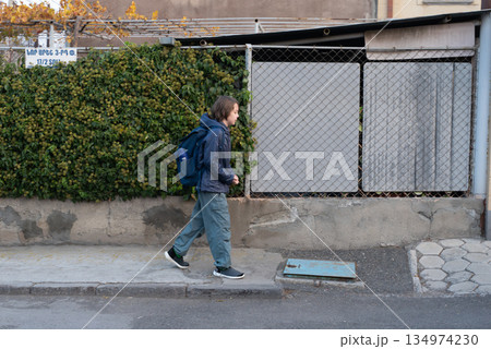 A young boy with a backpack walks to school on a city sidewalk. Student commuting A young boy with a backpack walks to school on a city sidewalk. Student commuting 134974230