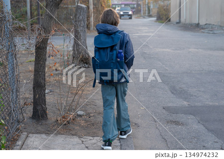 A student with a backpack walking away from the camera. Back view of a boy on a city street A student with a backpack walking away from the camera. Back view of a boy on a city street 134974232