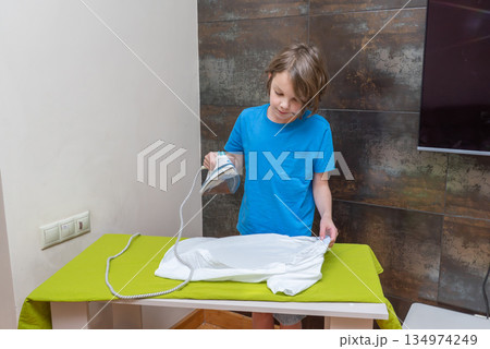Young boy ironing a white t-shirt at home. Child doing household chores and learning 134974249