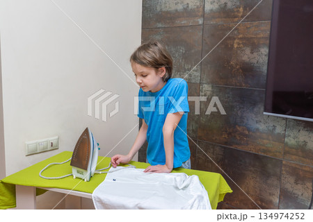Young boy learning to iron a white shirt at home. Child doing a household chore 134974252