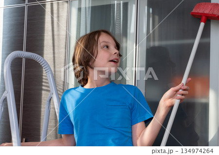 Young boy helping with household chores at home. Child cleaning with a red broom 134974264