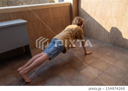 A young boy doing a push-up exercise on a balcony. Child's home workout for fitness A young boy doing a push-up exercise on a balcony. Child's home workout for fitness 134974268