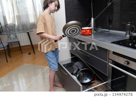 Young boy putting a frying pan away in a kitchen drawer. Household chores concept 134974278