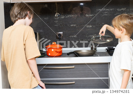 Two young boys cooking together in the kitchen. Child preparing a meal on the stove at home Two young boys cooking together in the kitchen. Child preparing a meal on the stove at home 134974281