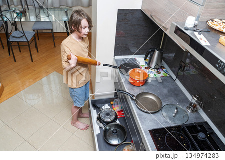 Young boy with a rolling pin in the kitchen. Child helping with cooking chores at home Young boy with a rolling pin in the kitchen. Child helping with cooking chores at home 134974283