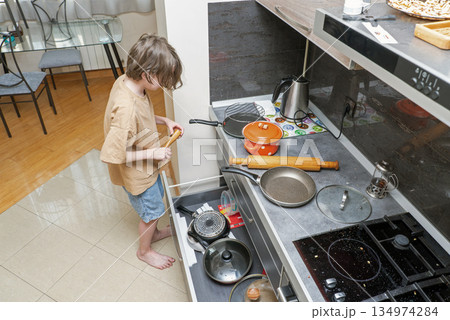 A young boy searching for cookware in an open kitchen drawer. Child helping at home A young boy searching for cookware in an open kitchen drawer. Child helping at home 134974284