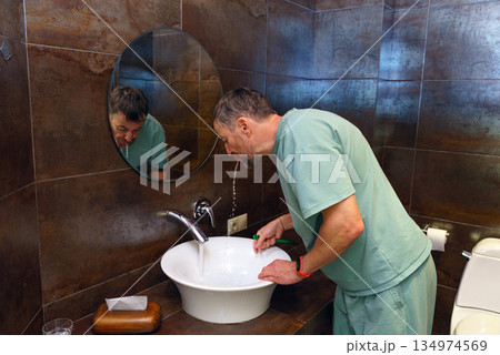 Middle-aged man rinsing his mouth over the sink in a bathroom. Morning dental hygiene routine 134974569