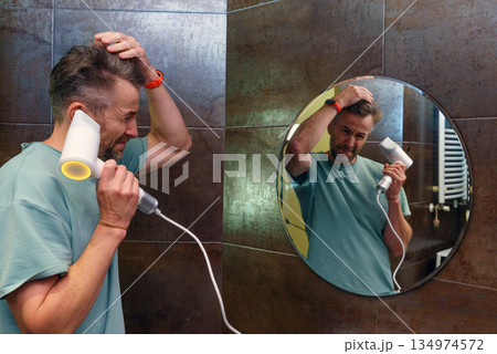 A man using a hairdryer in the bathroom. Daily grooming and self-care routine with mirror reflection 134974572