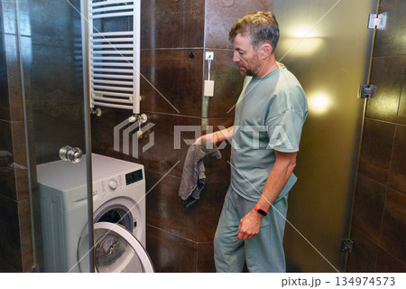 Middle-aged man preparing to wash clothes at home. Daily routine and domestic chores 134974573