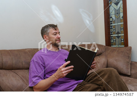 Casual man sitting on a sofa at home reading a book. Focused on learning and leisure 134974587