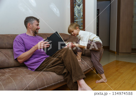 Father and son spending quality time at home. Man with a book on a couch interacting with his child 134974588