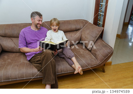 Excited boy and his father reading a storybook on a sofa. Family bonding time at home 134974589