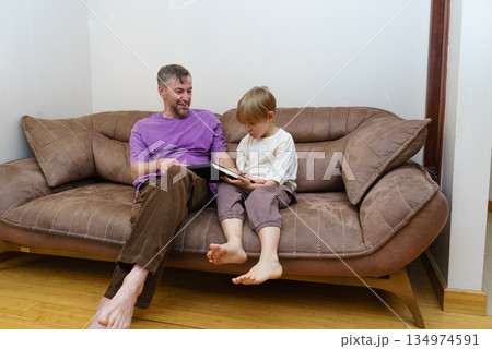 Father and son reading a book together on the couch. Family bonding and home education concept. Father and son reading a book together on the couch. Family bonding and home education concept. 134974591