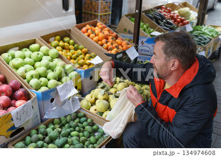 Man with a reusable bag choosing fresh quince at an outdoor farmers market. Healthy food shopping 134974608