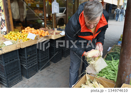 Man shopping for fresh corn at an outdoor farmers market. Customer choosing vegetables at a local stand Man shopping for fresh corn at an outdoor farmers market. Customer choosing vegetables at a local stand 134974610