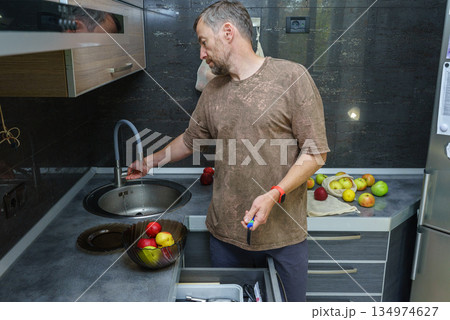 Man washing fresh apples in a modern kitchen sink. Healthy home lifestyle Man washing fresh apples in a modern kitchen sink. Healthy home lifestyle 134974627