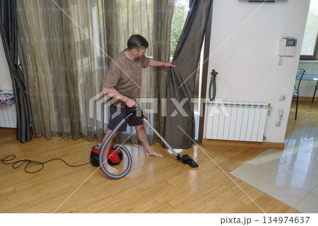 Barefoot man cleaning the wooden floor with a vacuum cleaner. Daily household chores Barefoot man cleaning the wooden floor with a vacuum cleaner. Daily household chores 134974637