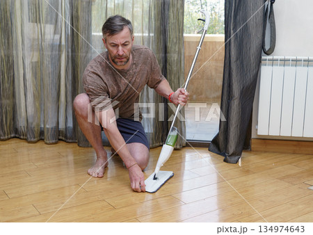 Man cleaning the wooden floor at home with a spray mop. Housework and domestic chores concept 134974643
