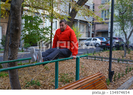 Man doing an L-sit exercise on parallel bars in an autumn park. Outdoor calisthenics workout 134974654